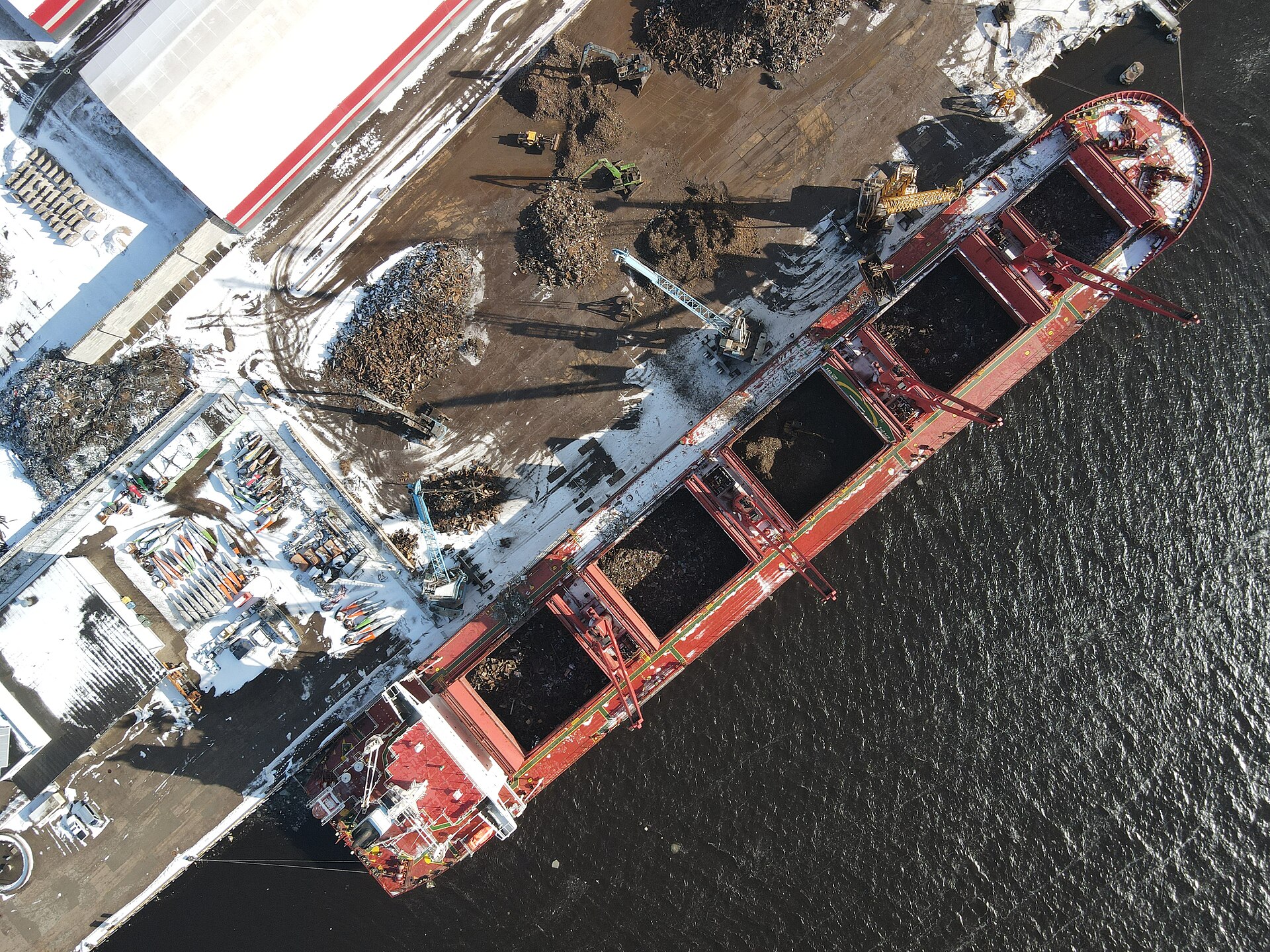 A geared bulk carrier handling metal scrap at a snow-covered quay