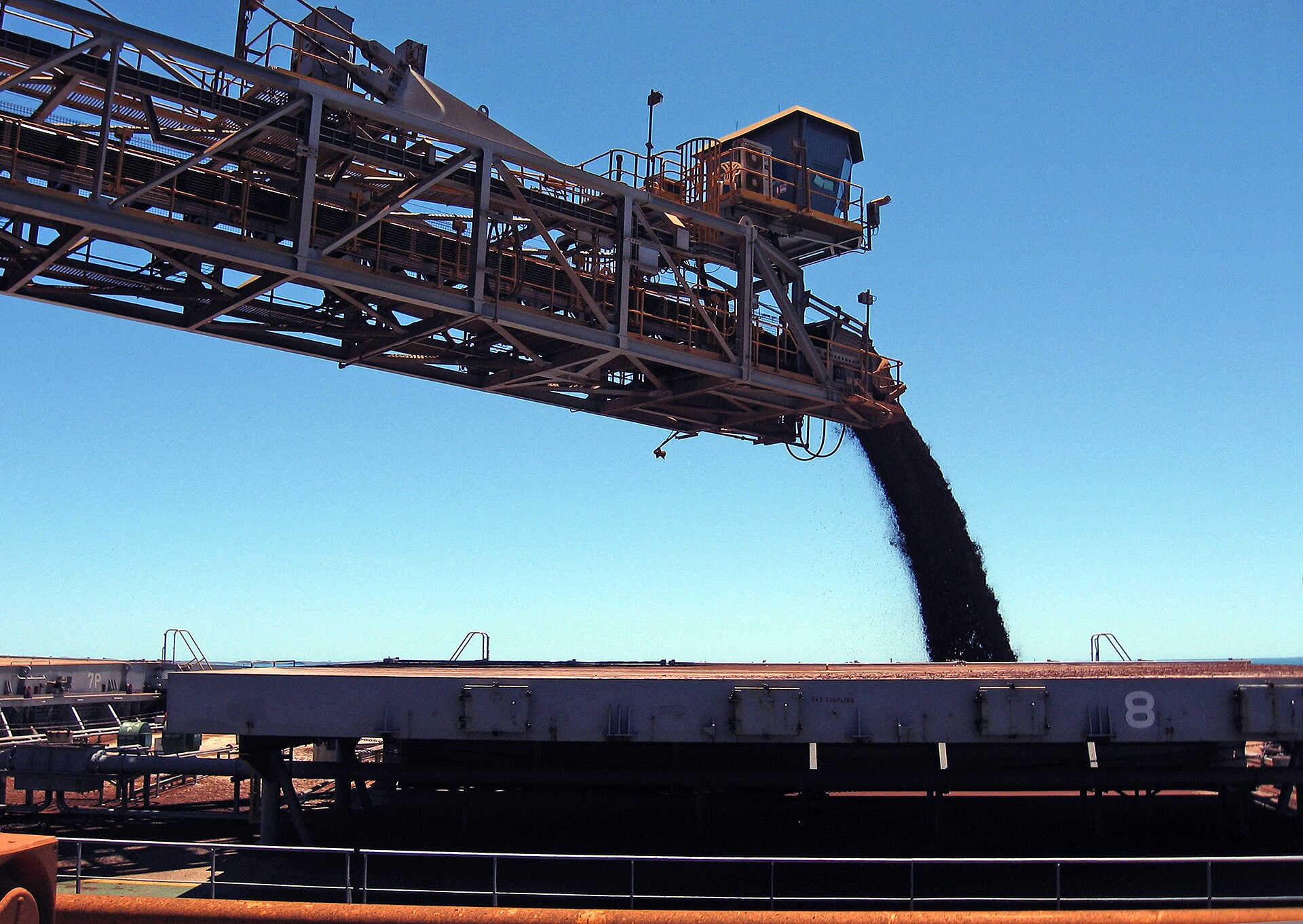 Close view of an iron ore shiploader delivering ore into a bulk carrier hold.